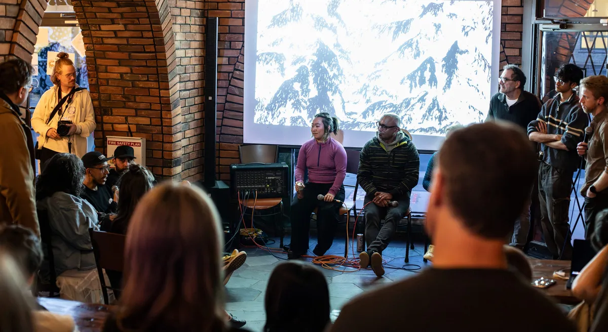 The opening artist Q&A at A/V Nights 2 — artists seated in front of a projected black-and-white film in a brick room, the audience packed in close around them.