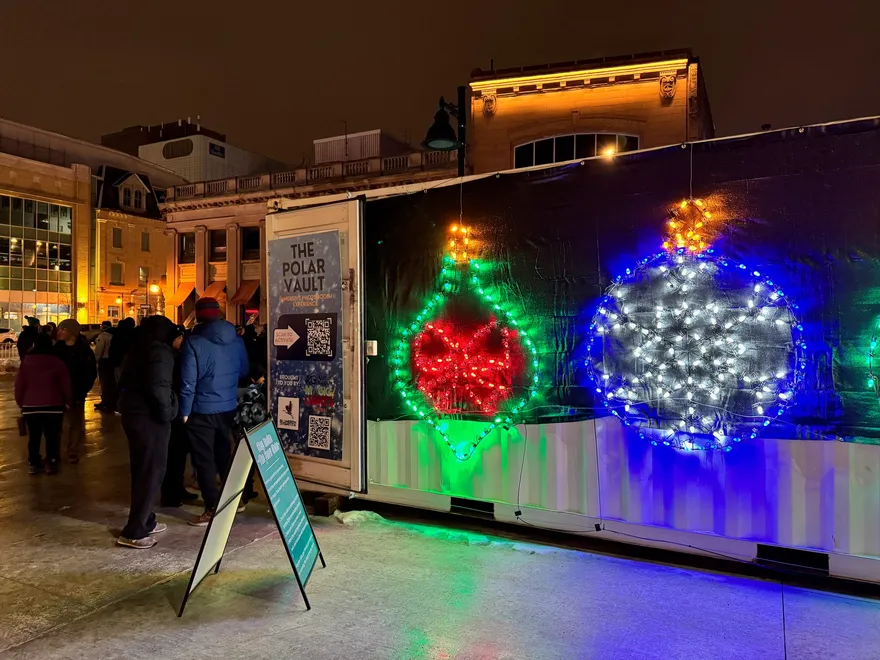 The Polar Vault container at night, lit with giant illuminated ornaments as visitors line up outside.