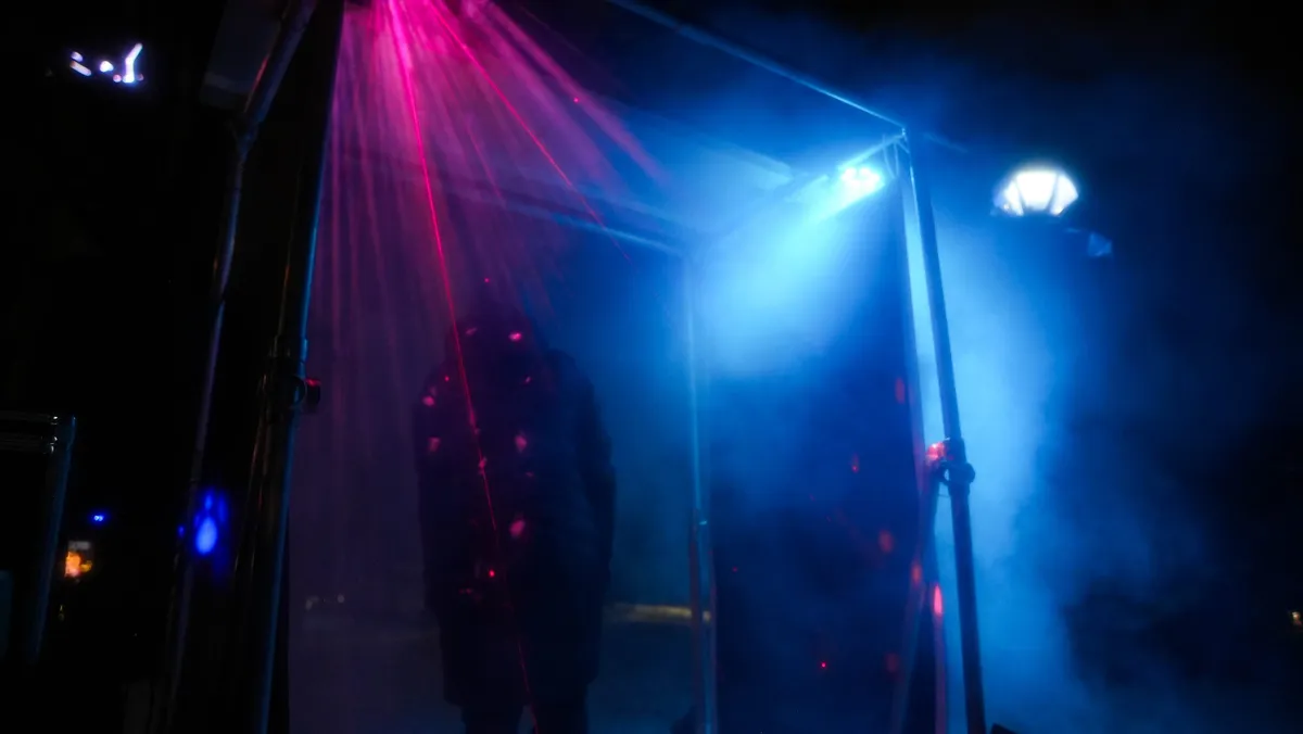 Magenta and blue laser light cutting through fog around the portal frame at night.