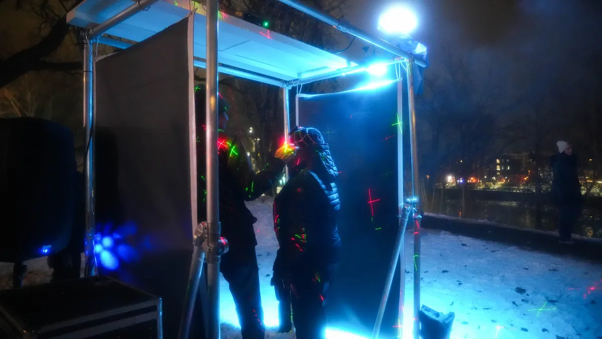 Two visitors passing through the illuminated portal as laser points scatter across them and the snow.